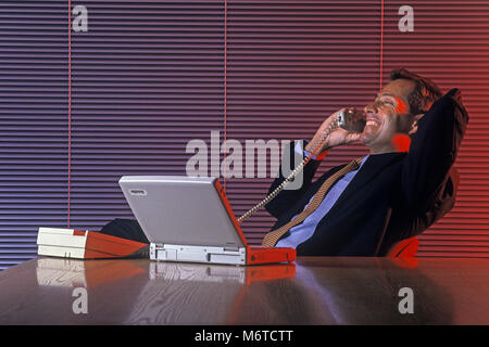 1994 caucasico storico BUSINESS MAN SUL TELEFONO A TAVOLA CON COMPUTER PORTATILE (©TOSHIBA CORP 1994) in OFFICE Foto Stock
