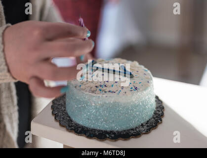 Macro closeup di mano mettendo la candela sulla torta per la prima celebrazione di compleanno Foto Stock