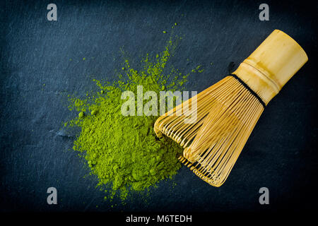 Cumulo di tè verde Matcha con frusta di bambù su ardesia scura, sfondo top-view, close-up. Foto Stock