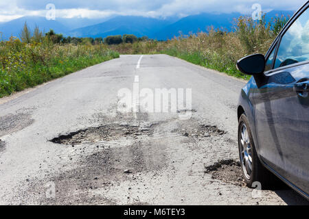 Auto e Asfalto Screpolato con fori in strada Foto Stock