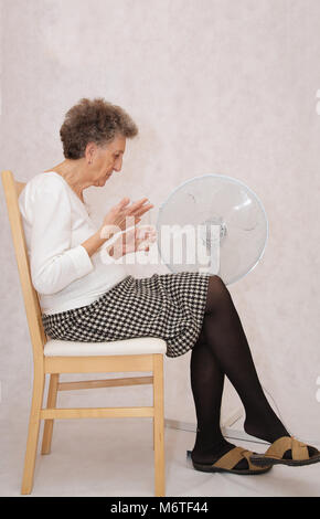 Senior donna tra 70 e 80 anni resta vicino al ventilatore. Soffre di calore Foto Stock