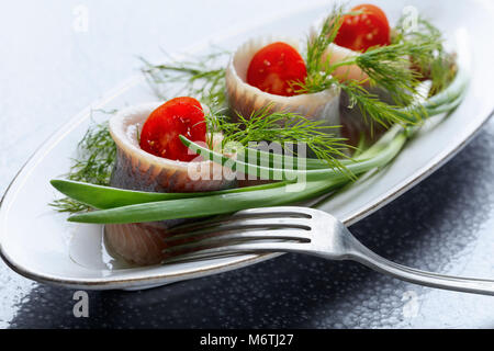 Il Filetto di aringa in olio. Rotoli con aneto , cipolla verde e pomodori ciliegia . Foto Stock