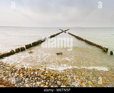 I frangiflutti in legno su una spiaggia del Mar Baltico con un sole nascosto in nuvole basse. Regolare il livello di acqua dopo la tempesta. Foto Stock