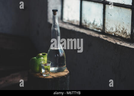 Apple brandy, rustica atmosfera rétro. Bottiglia e unico colpo di vetro con alcool bere e due verde mela frutta. Foto Stock