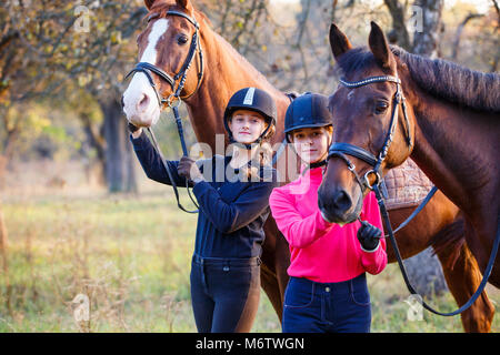 Due ragazze adolescenti con i loro cavalli nel parco d'autunno. Sport Equestri sfondo con spazio di copia Foto Stock