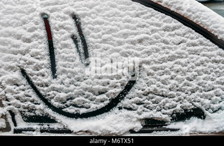 Sfondo di neve. Texture di neve bagnata con un allegro smiley modello di simbolo nella finestra invernale della vettura all'aperto di close-up. Smile nella neve, felice allegro immagine. Foto Stock