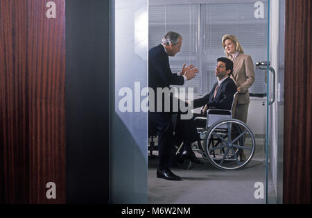 1995 STORICO BUSINESS caucasica uomo che parla al disabile business uomo seduto nella sedia a rotelle IN UFFICIO Foto Stock