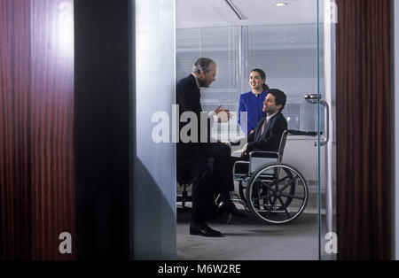 1995 STORICO BUSINESS caucasica uomo che parla al disabile business uomo seduto nella sedia a rotelle IN UFFICIO Foto Stock