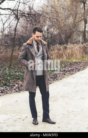 Bello ed elegante uomo nel parco indossare tuta e ricoprire. Foto Stock