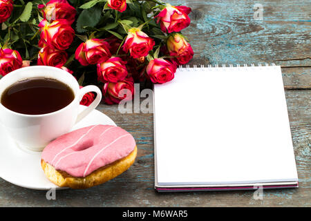Tazza di tè con donut , rose fresche , notebook e il foglio di carta su sfondo di legno per la Festa della mamma. Foto Stock