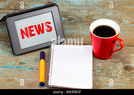 News iscrizione sul tablet schermo. Tablet PC con aprire il notebook e la tazza di caffè sullo sfondo di legno. Foto Stock