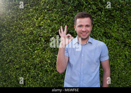 Un sorridente uomo caucasico mostra ok segno, sulla verde erba di eco Foto Stock