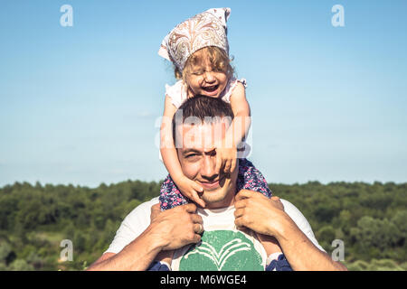 Padre figlia carino avere divertimento insieme come famiglia lifestyle ritratto nella parte anteriore del cielo blu. Padre Felice Tiene il suo bambino sulla spalla Foto Stock