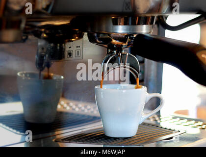 Una macchina espresso gocciola caffè ricco in una tazza bianca. Foto Stock