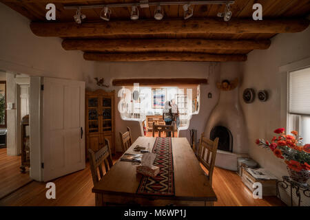 Una pittoresca Santa Fe, New Mexico sala da pranzo in un adobe architettura stile casa con pavimenti in legno, log dei soffitti e pareti bianche. Foto Stock