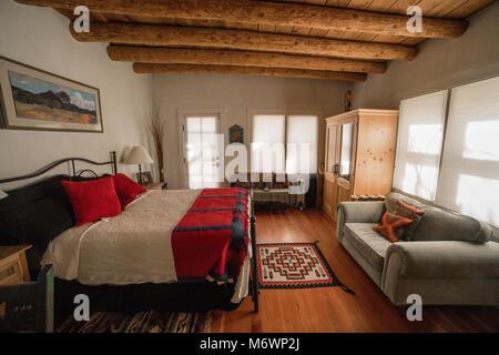 Una pittoresca Santa Fe, New Mexico camera da letto in un adobe architettura stile casa con pavimenti in legno, log dei soffitti e pareti bianche. Foto Stock