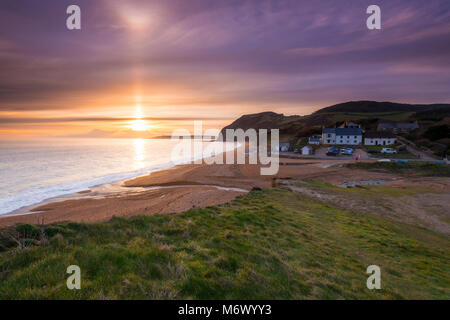 Seatown, Dorset, Regno Unito. Il 6 marzo 2018. Regno Unito Meteo. Un fascio di luce del sole splende alto sul livello alto nuvole che sono parzialmente oscurando il tramonto a Seatown su Jurassic Coast di Dorset. Nella foto è lo storico pub la Anchor Inn. Credito Foto: Graham Hunt/Alamy Live News Foto Stock