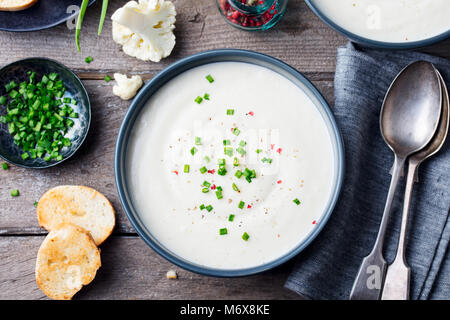 Il cavolfiore, crema di patate zuppa di cipolla verde in vaso nero su grigio Sfondo di legno. Foto Stock