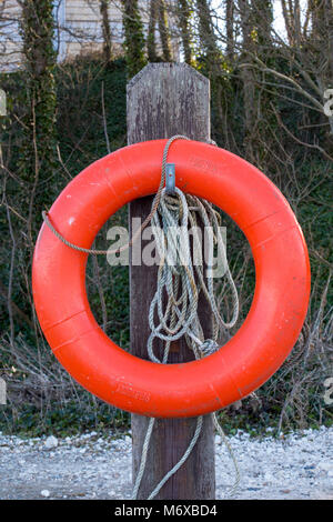 Un arancione perry boa o salvagente anello di gomma o dispositivo di galleggiamento per lifesaving in prossimità di acqua su un palo di legno con una corda fissata per il lancio di acqua Foto Stock