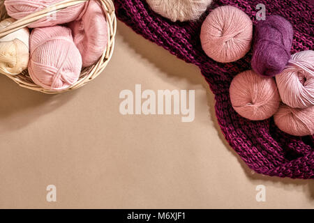 Palline di filato e aghi da maglia. Filato colorato per lavorazione a maglia in un recipiente di vimini su un sfondo beige. Foto Stock