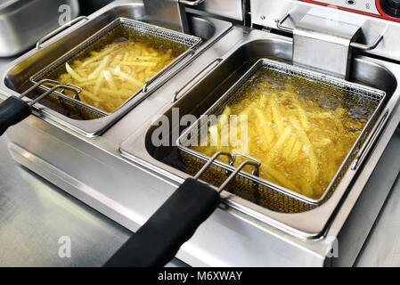 Le patatine fritte o patatine friggere in olio in un metallo commerciale friggitrice in un ristorante come accompagnamento ai pasti Foto Stock