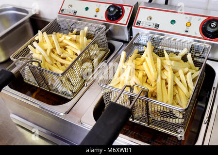 Dorate e croccanti patatine svuotamento in filo cesti di metallo su un elettrico friggitrice nella cucina di un ristorante Foto Stock
