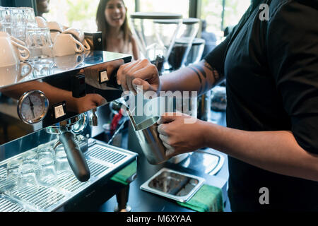 Mano di un barista tenendo una tazza in acciaio inox Foto Stock