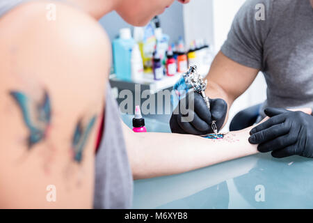 Close-up delle mani di un esperto tattoo artist indossando guanti neri Foto Stock