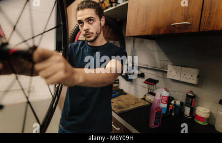 Uomo al lavoro su di una ruota di bicicletta in un negozio di riparazione. Lavoratore allineamento di una ruota di bicicletta in officina. Foto Stock