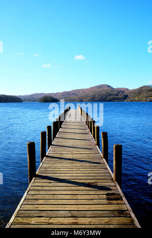 Lungo rettilineo simmetrico bellissimo piede legno pontile proteso oltre un calmo lago blu, con colline verdi campi e boschi della Foresta in backgrou Foto Stock