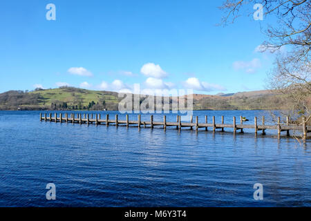 Un lungo rettilineo bellissimo piede legno pontile proteso oltre un calmo lago blu, con colline verdi campi e boschi della Foresta di sfondo, la s Foto Stock