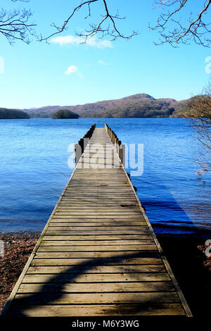 Lungo rettilineo simmetrico piede legno pontile proteso oltre un calmo lago blu, con colline verdi campi e boschi della Foresta in background, il su Foto Stock