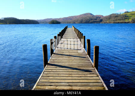 Lungo rettilineo simmetrico piede legno pontile proteso oltre un calmo lago blu, con colline verdi campi e boschi della Foresta in background, il su Foto Stock