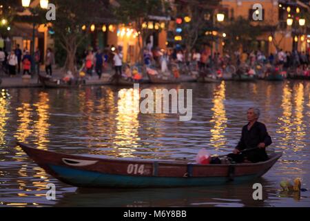 Un anziano uomo locale pagaie la sua barca lungo il fiume Thu Bon, con Bach Dang Street in background Foto Stock