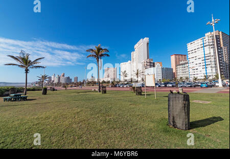 Prato verde, pavimentato promenade e alberi di palma contro blu nuvoloso Durban skyline della città in Sud Africa Foto Stock