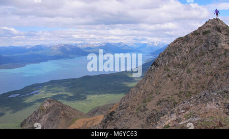 Tanalian Mountain . Un singolo escursionista si erge vittorioso sulla cima della montagna Tanalian, affacciato sul turchese del lago Clark Foto Stock