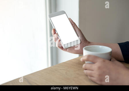 Mockup immagine di mani white telefono cellulare con schermo vuoto con una tazza di caffè sul tavolo di legno in cafe Foto Stock