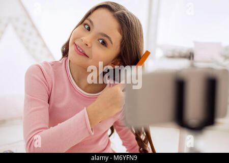 Ragazza carina spazzolare i capelli durante le riprese di tutorial Foto Stock