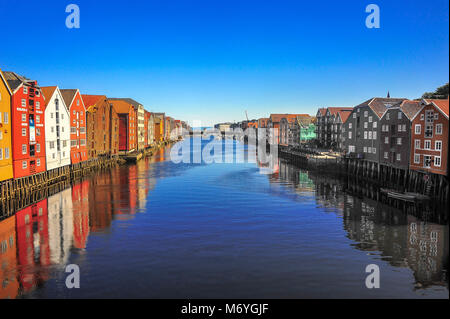 Storico di magazzini di legno allineate sulle rive del fiume Nidelva a Trondheim, Norvegia. Scena colorati, cielo blu chiaro, ancora acqua, riflessioni Foto Stock