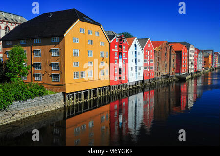 Storico di magazzini di legno allineate sulle rive del fiume Nidelva a Trondheim, Norvegia. Rossi, gialli e bianchi edifici, acque calme, cielo blu sullo sfondo Foto Stock