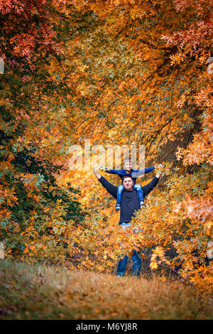 Padre dando figlio piggyback ride in autunno park Foto Stock