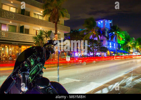 Ocean Drive a Miami la notte con vivaci colori di strada. Auto passando per la creazione di linee di luce durante una lunga esposizione. Bici in primo piano. Foto Stock