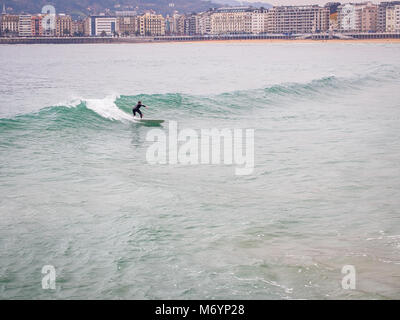 Lonely surfer è navigare su wawes presso la Concha Beach in San Sebastian, Paesi Baschi Foto Stock