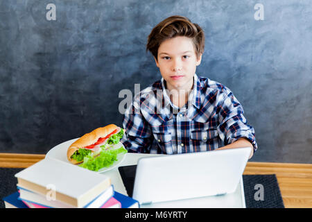 Ritratto di ragazzo adolescente mangia un panino e la navigazione sul web Foto Stock