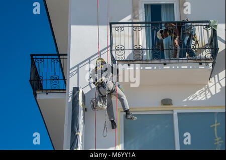 L'uomo la discesa in corda doppia verso il basso il lato di un edificio la verniciatura esterna, accesso con cordami. Foto Stock