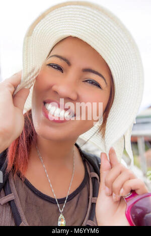 Bella donna filippina della modellazione di un ampio orlo white hat. Ella ha carnagione chiara, largo sorriso toothy e indossa il trucco. Foto Stock