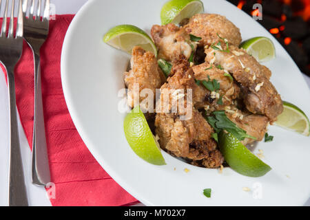 Un Frango passarihno, un brasiliano piatto di fritto di pollo a pezzi in calce e aglio servita con spicchi di lime e prezzemolo fresco tritato Foto Stock