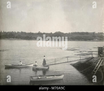 Antique circa 1905 fotografia, donne sul dock e uomo in canotto sul fiume Sasanoa. La posizione è in o vicino a Riggsville (ora Robinhood), Maine in Sagadahoc County, Stati Uniti d'America. Foto Stock