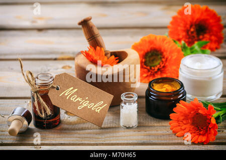 Calendula o fiorrancio prodotti. Olio essenziale, globuli di omeopatia e cosmetici, tag con testo calendula. Tavolo in legno sfondo Foto Stock