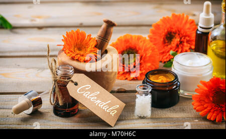 Calendula o fiorrancio prodotti. Olio essenziale, globuli di omeopatia e cosmetici, tag con testo calendula. Tavolo in legno sfondo Foto Stock